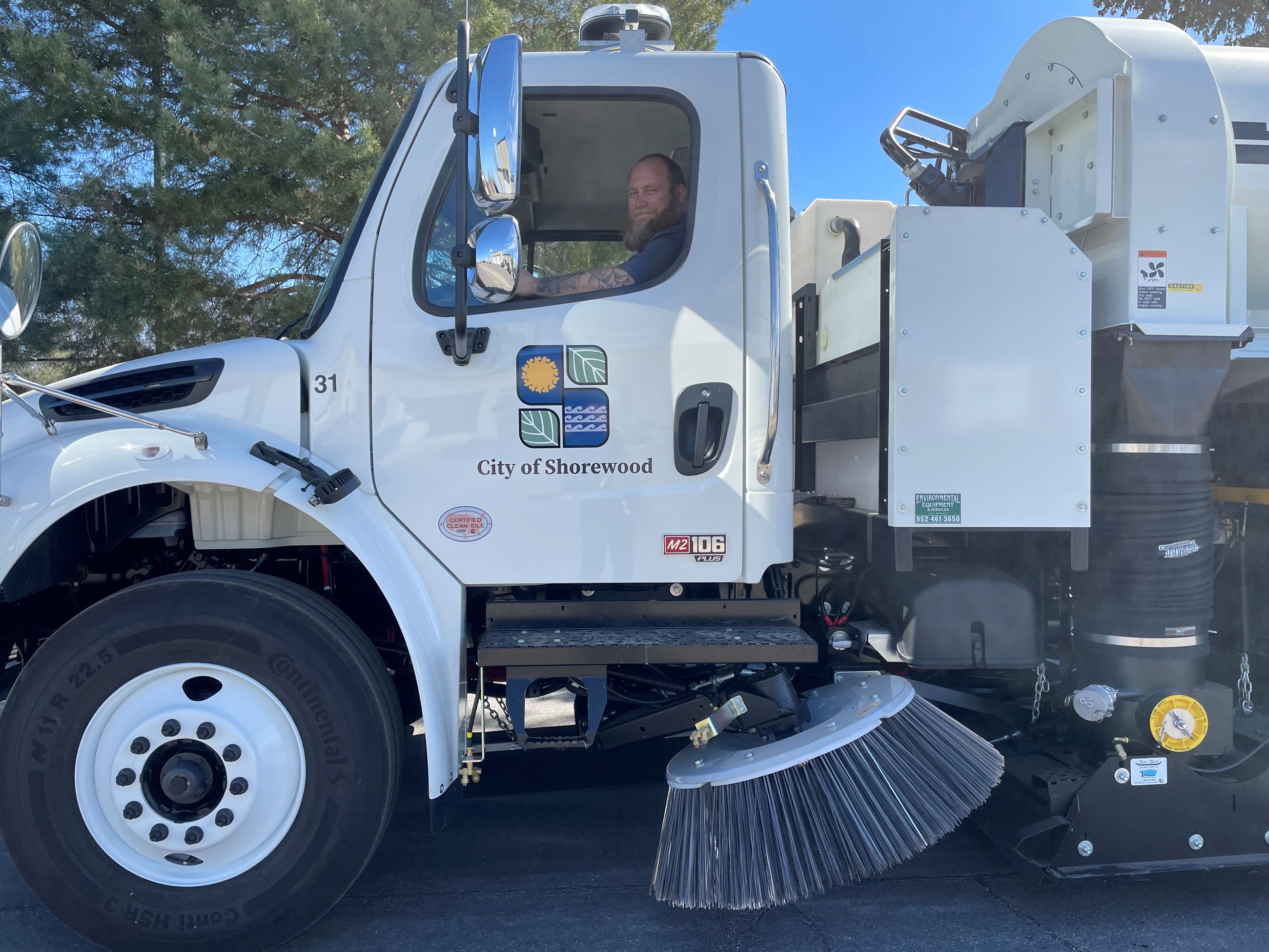man with beard smiling at camera, sitting in large, white street sweeper truck